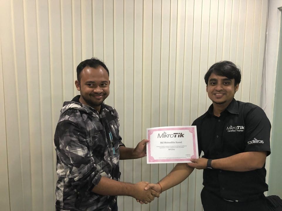 Titas Sarker, wearing a MikroTik Certified Trainer shirt, handing an MTCNA certificate to a student