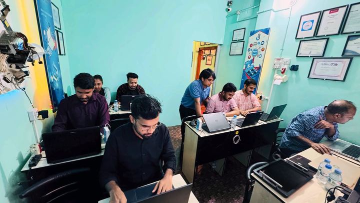 Trainer in a blue shirt leaning over to help a student at a laptop
