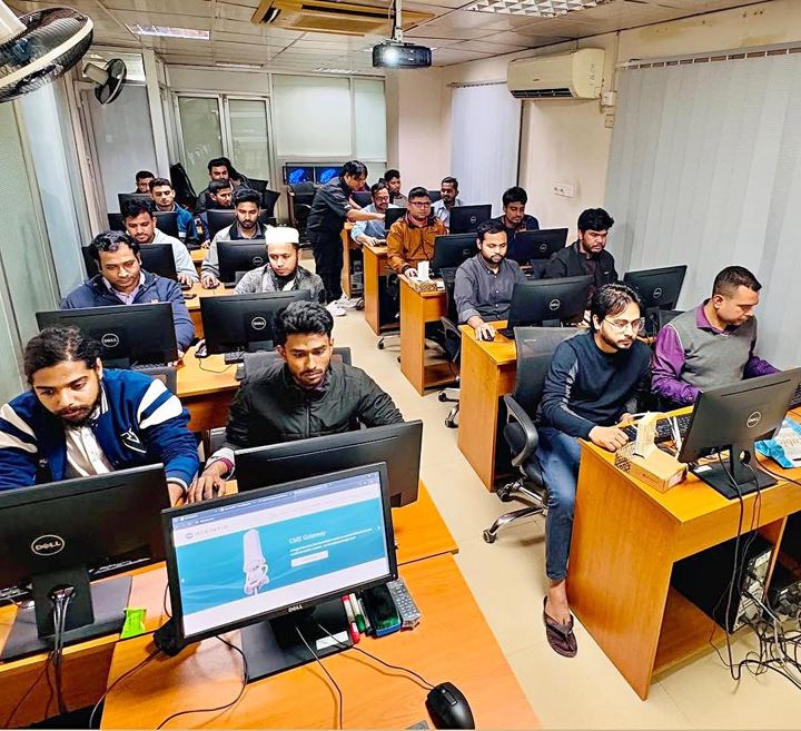 Rows of students working on desktop computers while the trainer helps a participant