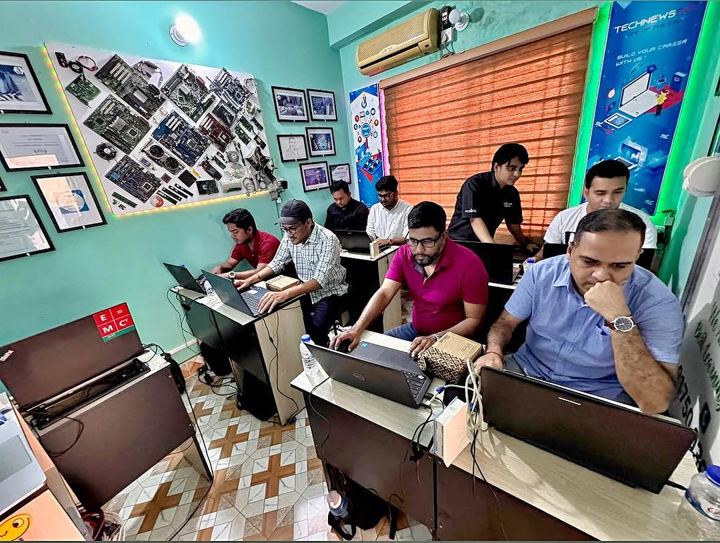 Trainer standing behind students working on laptops in a teal-walled classroom